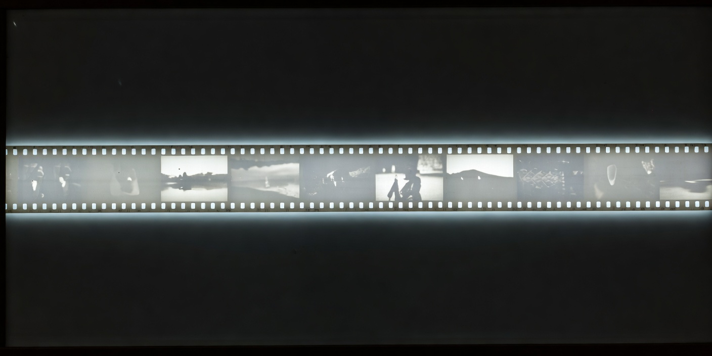 A strip of 35mm film lying across a light table, frames glowing against a black surround